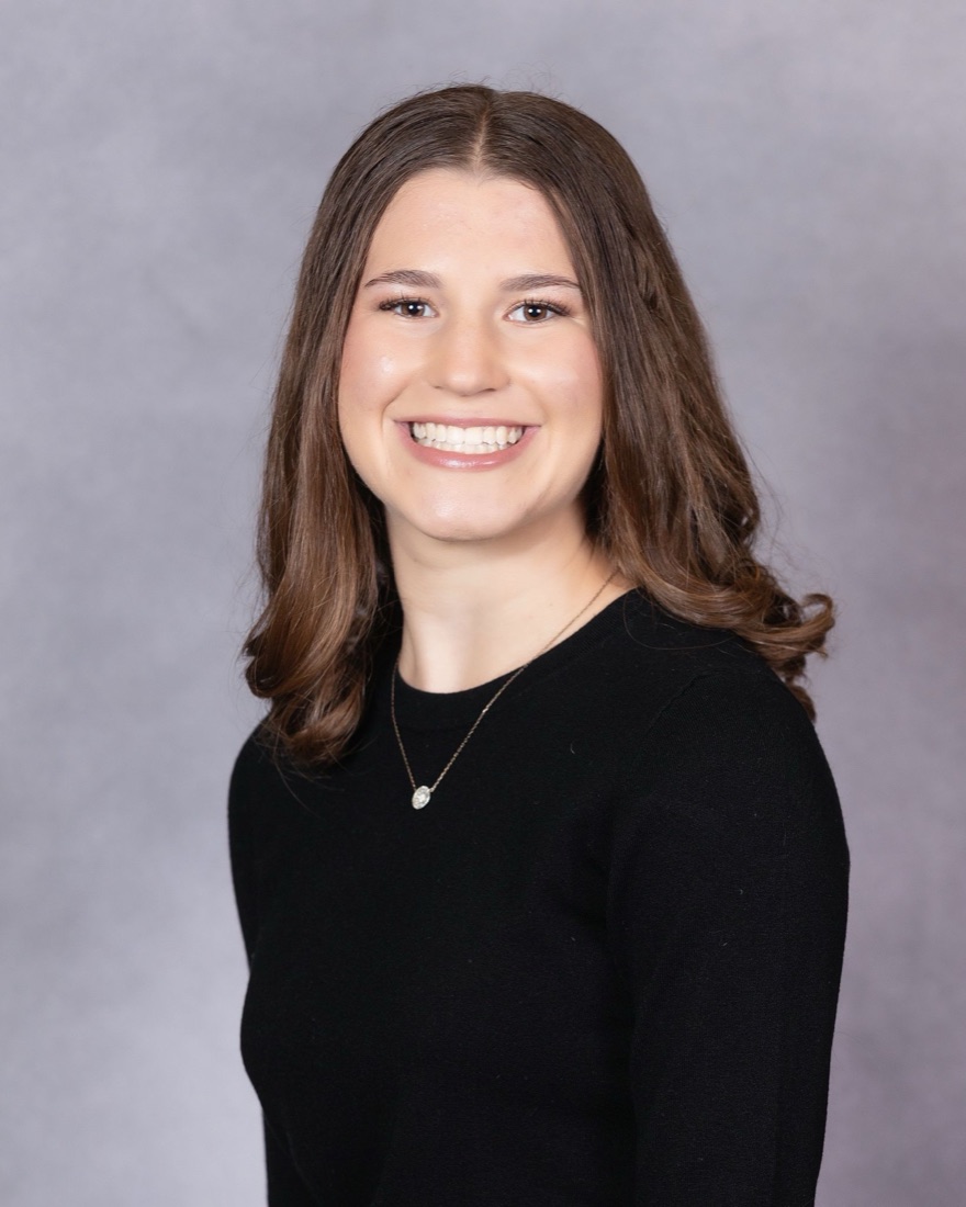Hannah Friedman, smiling, in a black top against a grey studio backdrop.
